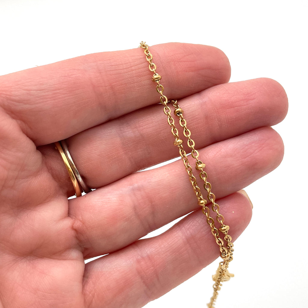 golden satellite chain bracelet shown on a hand against a white background. 