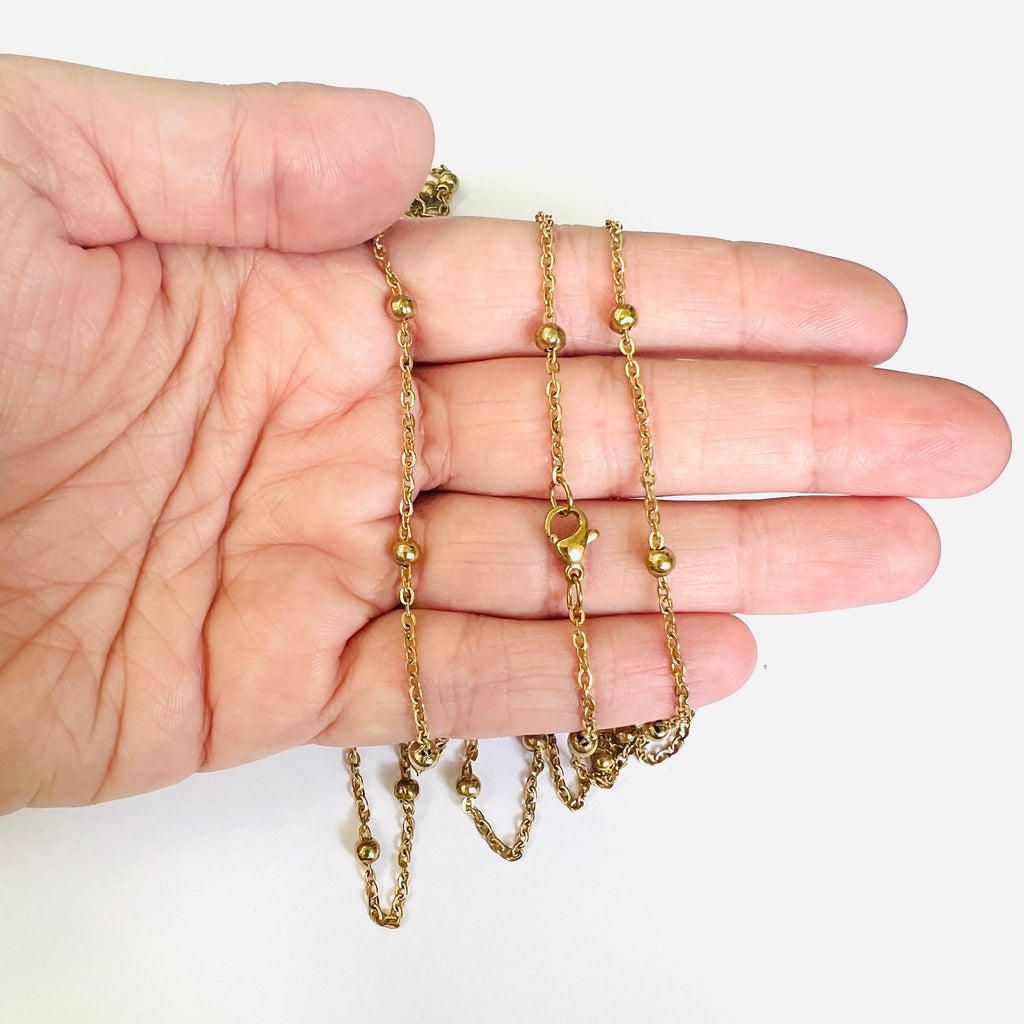 golden large bead satellite chain necklace with lobster claw clasp displayed on a hand with white background. 