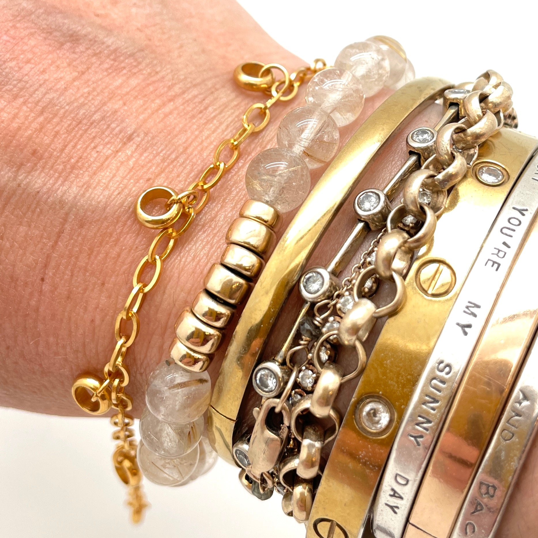 golden add-a-charm bracelet with  evenly spaced, dangling, soldered jump rings displayed on a bracelet stacked wrist against a white background. 