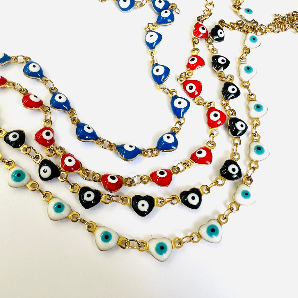 4 golden enamel heart shaped evil eye  necklaces displaying available enamel heart color options starting with blue above red above black above white on a white background. 