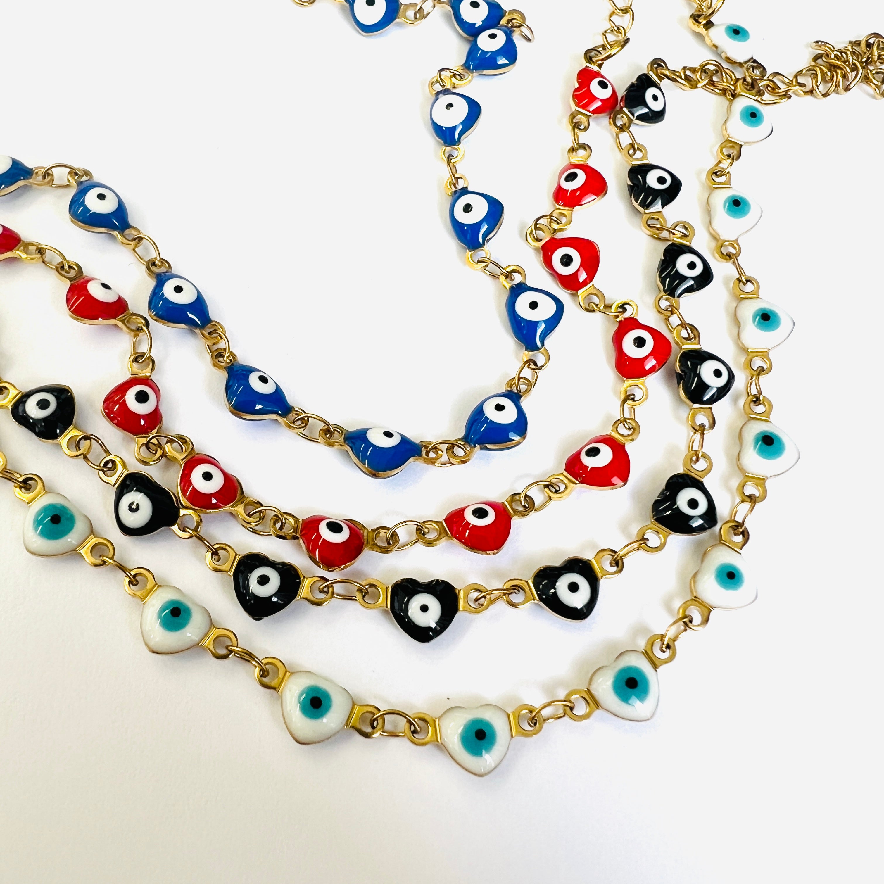 4 golden enamel heart shaped evil eye  necklaces displaying available enamel heart color options starting with blue above red above black above white on a white background. 
