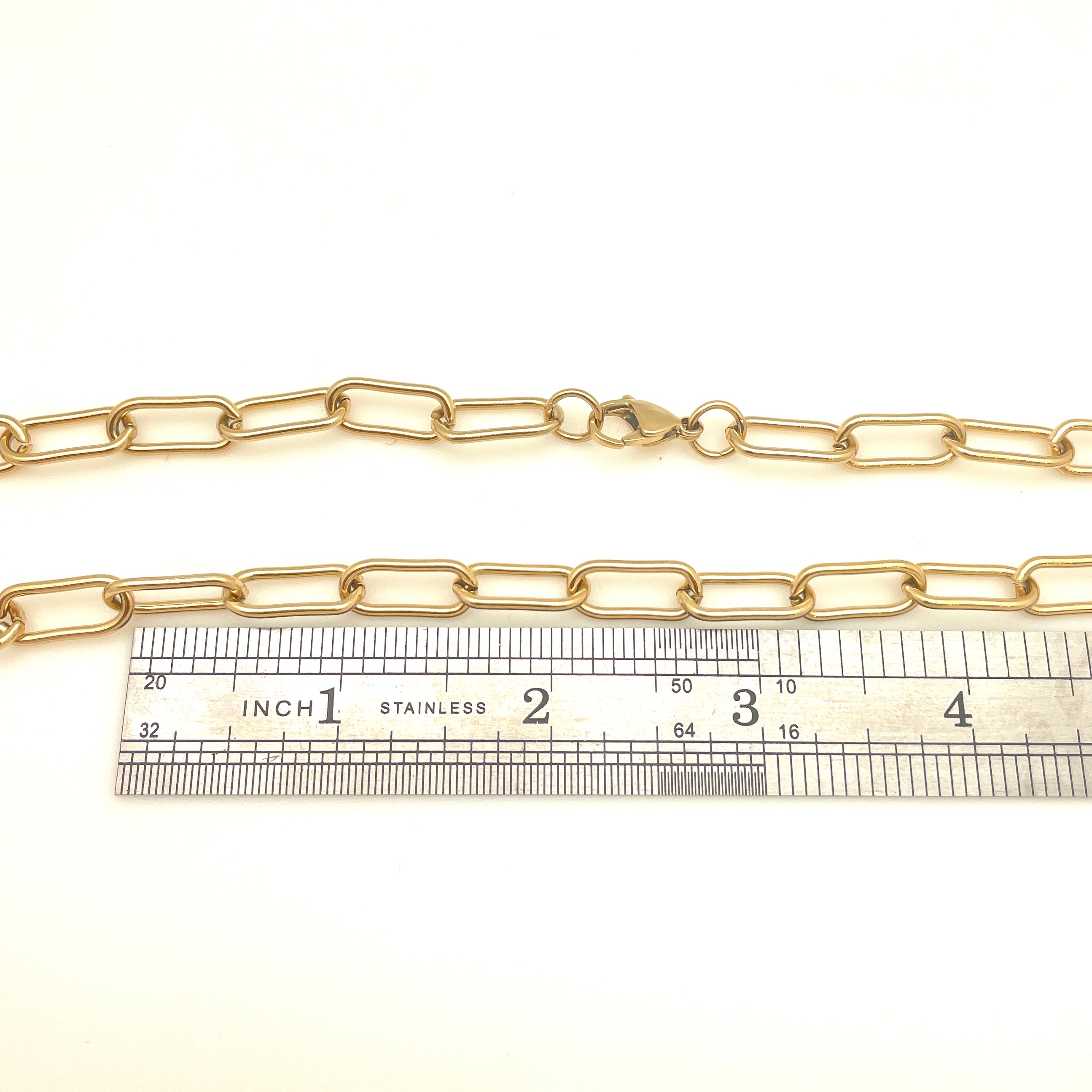 golden large round paperclip chain necklace with large lobster claw clasp displayed above ruler over white background. 