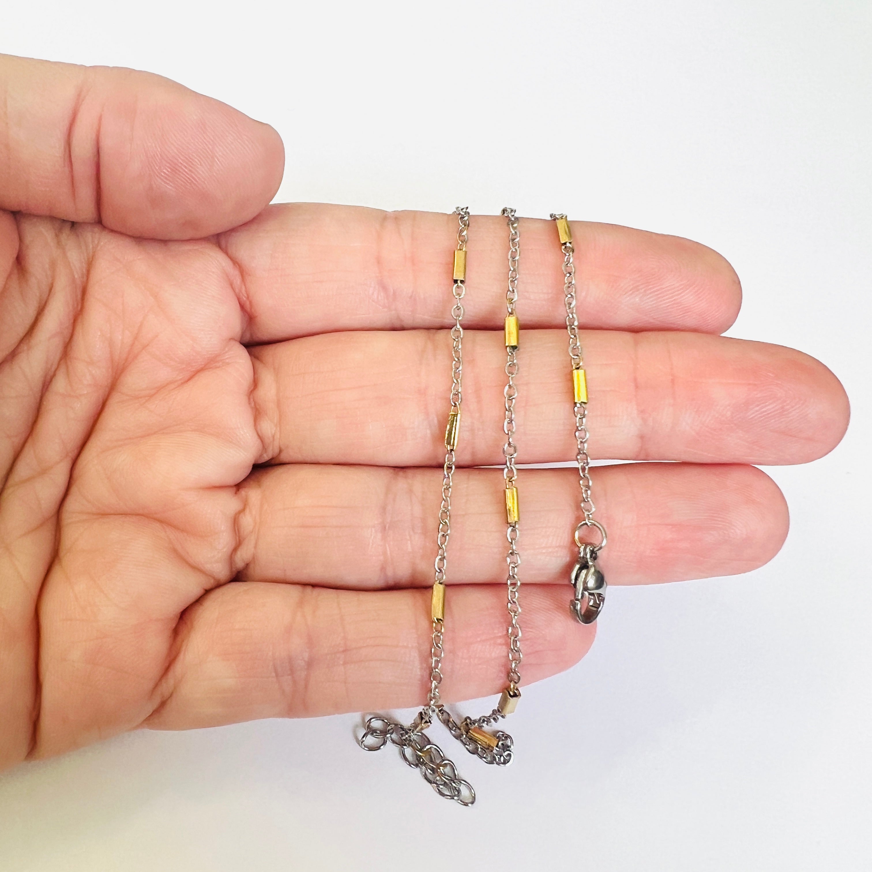 a couple silver tone cable chain satellite bracelets with golden bar link stations and lobster claw clasps draped over hand with white background. 