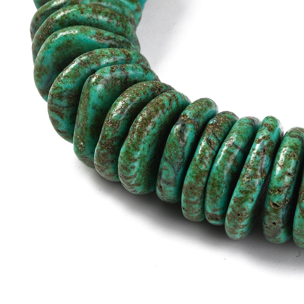 close-up of graduated dark green dyed synthetic turquoise bead strand over white surface. 
