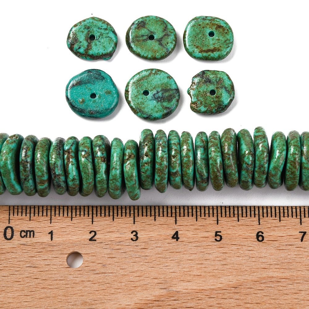 dark green dyed, synthetic turquoise graduated bead strand with six loose beads above and a wooden ruler below all on a white surface.