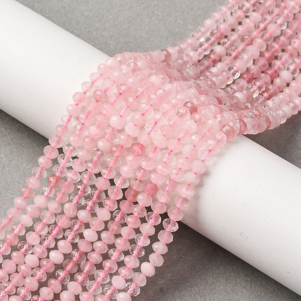 faceted rondelle rose quartz bead strands draped over white cylinder form onto grey felt surface.