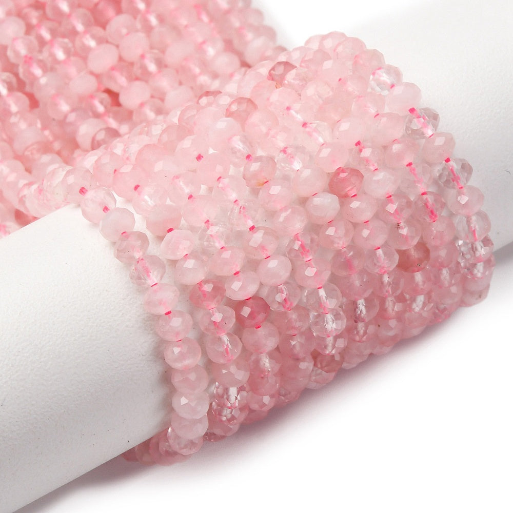 faceted rondelle rose quartz bead strands wrapped around white cylinder form over white surface. 