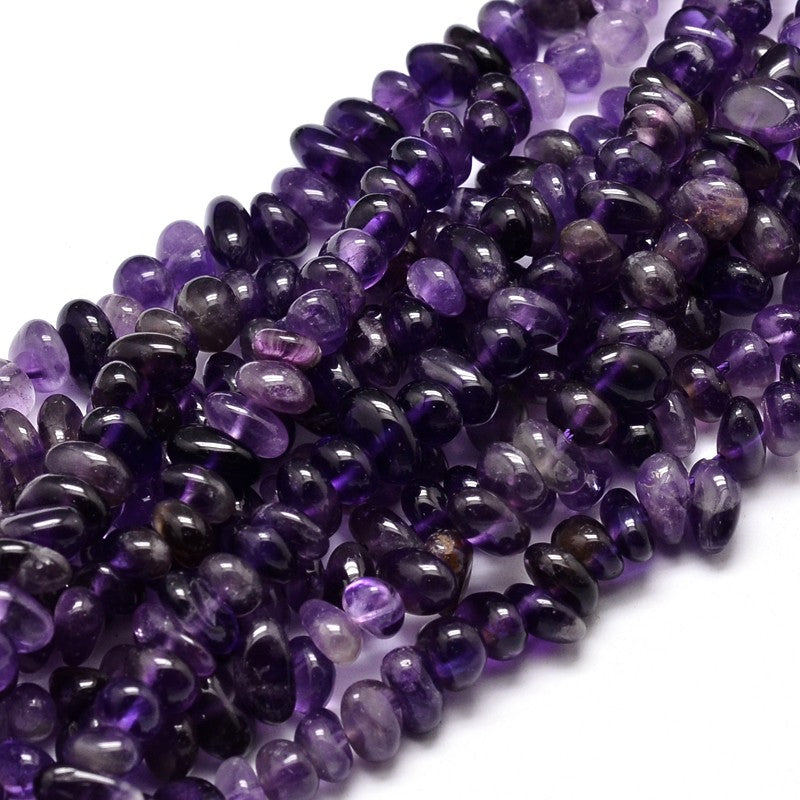 many tumbled amethyst nugget chip bead strands twisted together over white surface. 