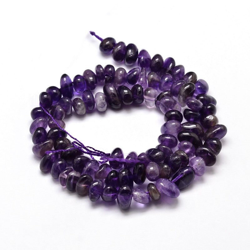tumbled amethyst nugget chip bead strand in a swirl design over white surface. 
