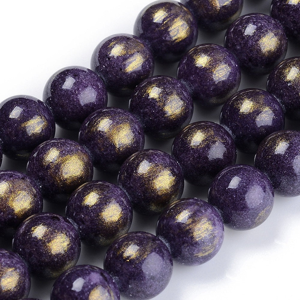zoomed in sections of smooth round and dyed purple jade bead strands with gold foil over a white surface. 