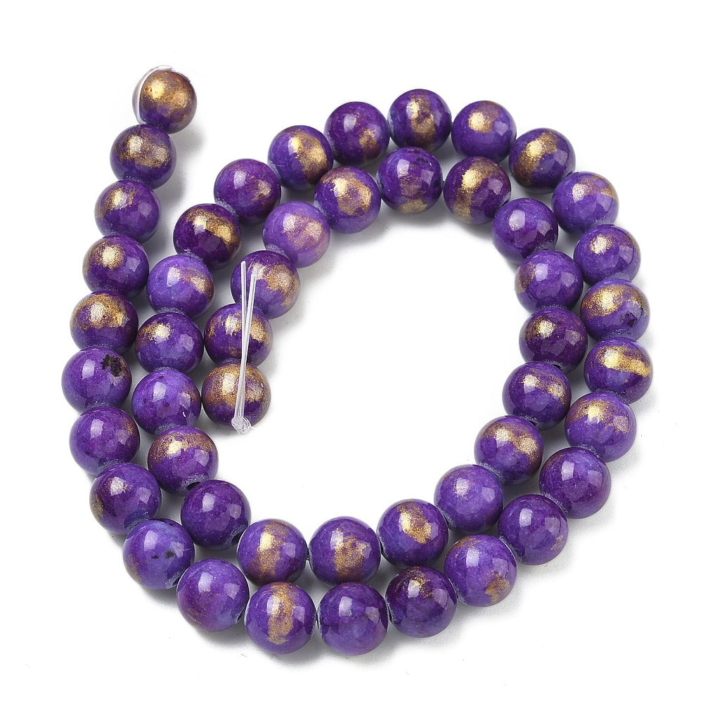 smooth round and dyed purple jade bead strand with gold foil in a swirl display over white surface. 