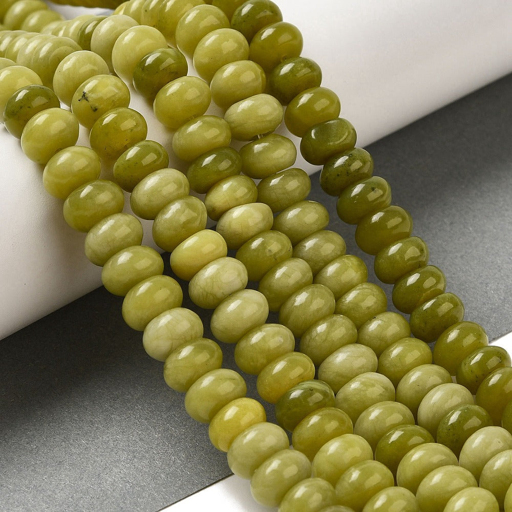 light olive dyed jade rondelle strands draped over white ledge onto grey surface.