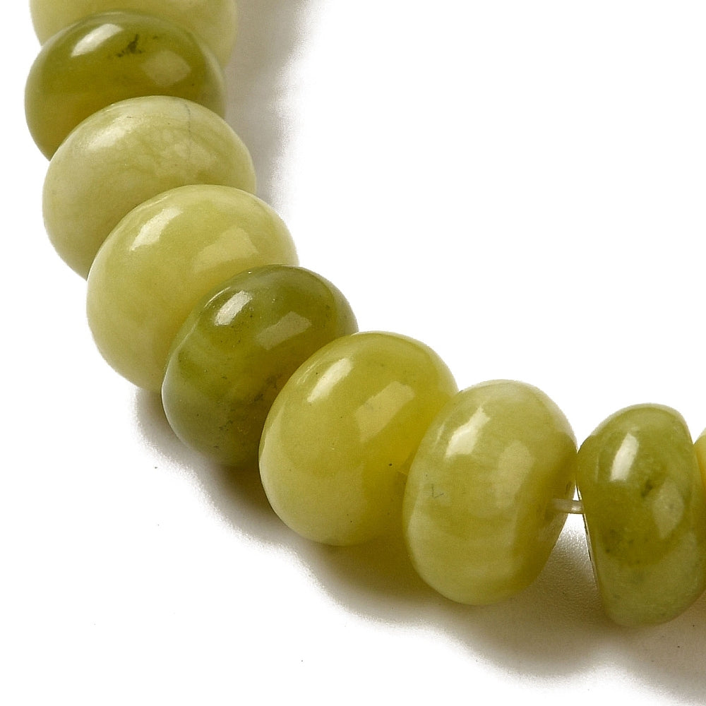 zoomed in section of light olive dyed jade rondelle strand over white surface. 