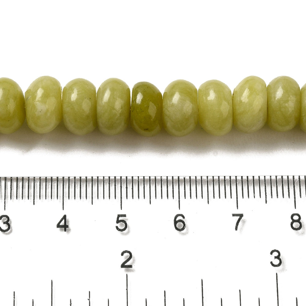 zoomed in section of light olive dyed jade rondelle strand above clear ruler over white surface. 