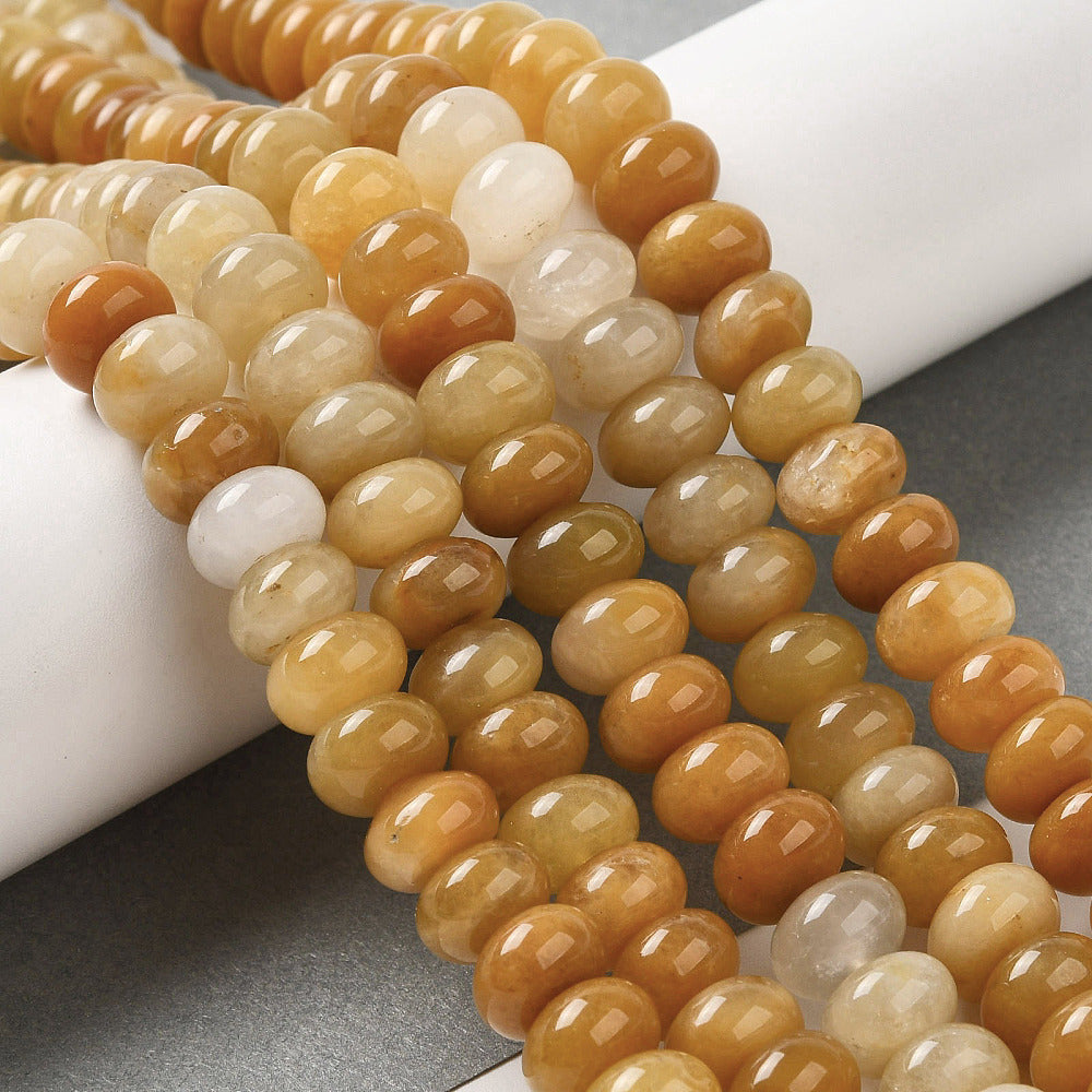 assorted dark yellow dyed jade rondelle strands draped over white ledge onto grey surface.