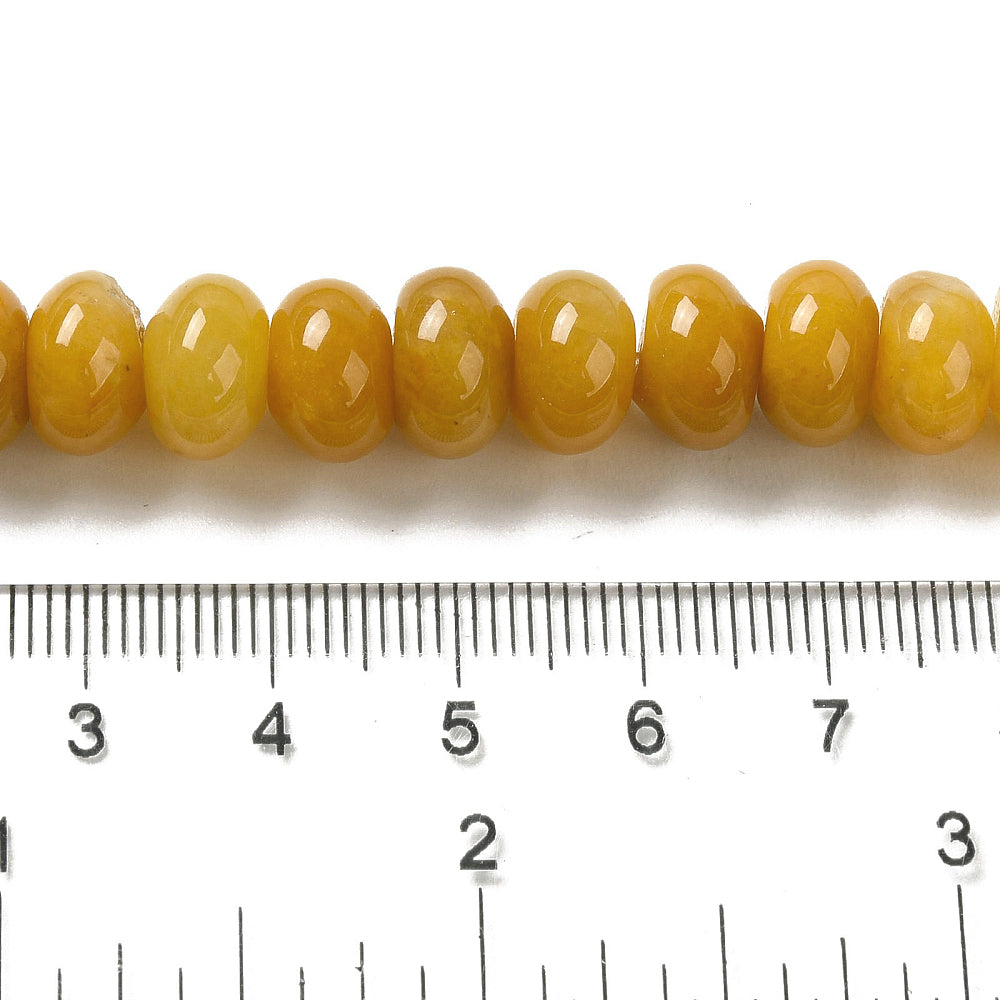 zoomed in section of assorted dark yellow dyed jade rondelle strand above clear ruler over white surface. 