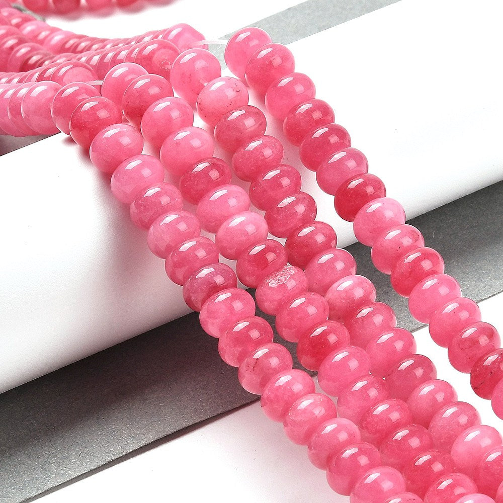 pink dyed jade rondelle strands draped over white ledge onto grey surface.