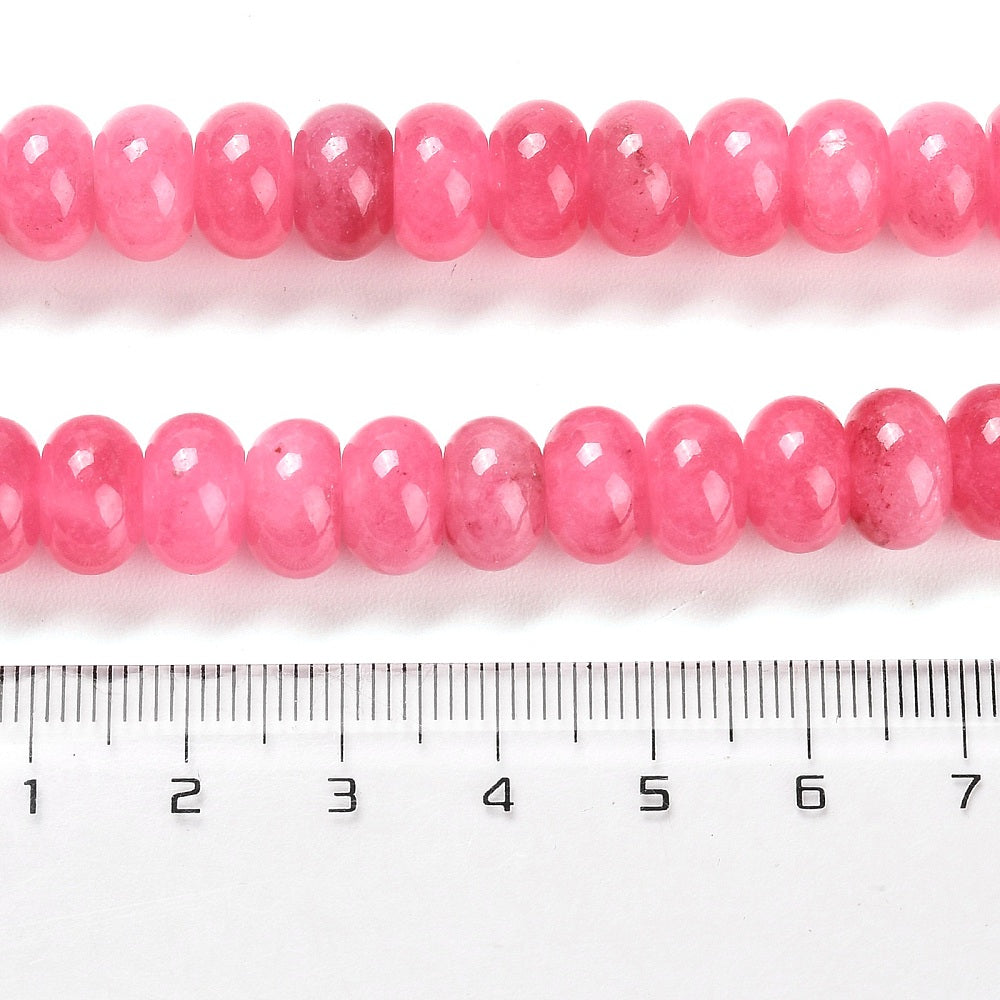 zoomed in sections of pink dyed jade rondelle strand above clear ruler over white surface. 