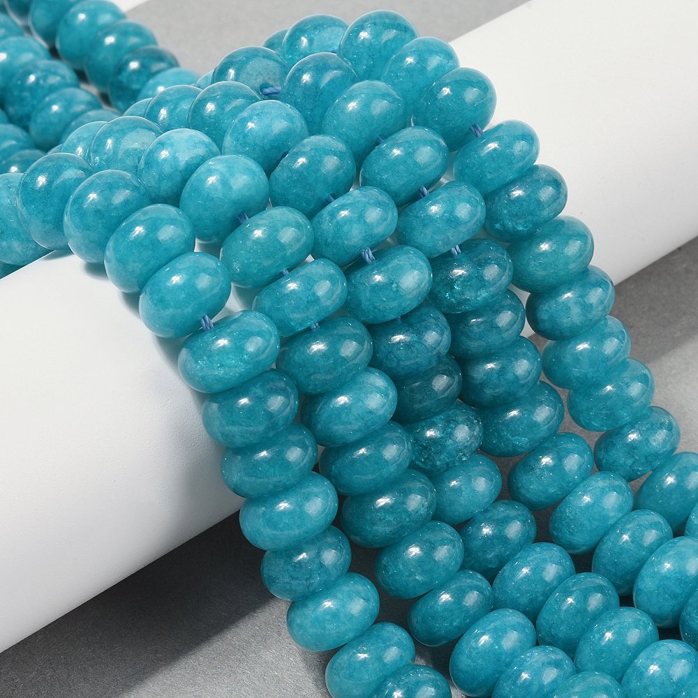 teal dyed jade rondelle strands draped over white ledge onto grey surface.