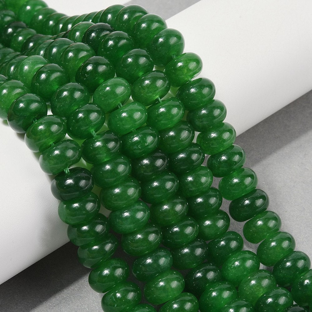 dark green dyed jade rondelle strands draped over white ledge onto grey surface.