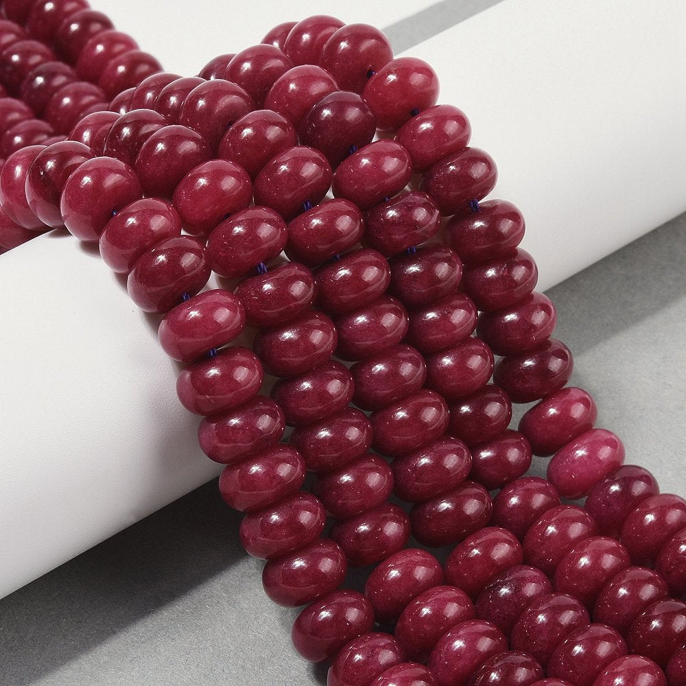 dark red dyed jade rondelle strands draped over white ledge onto grey surface.