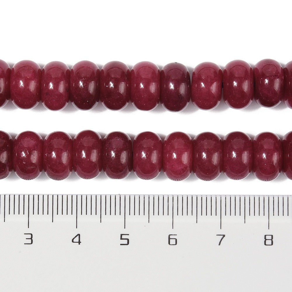 zoomed in sections of dark red dyed jade rondelle strand above clear ruler over white surface. 