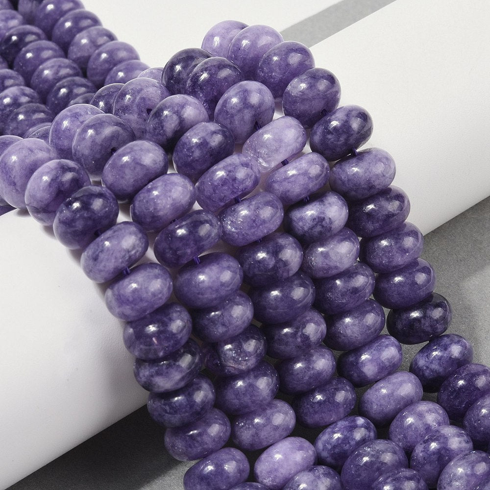 light purple dyed jade rondelle strands draped over white ledge onto grey surface.