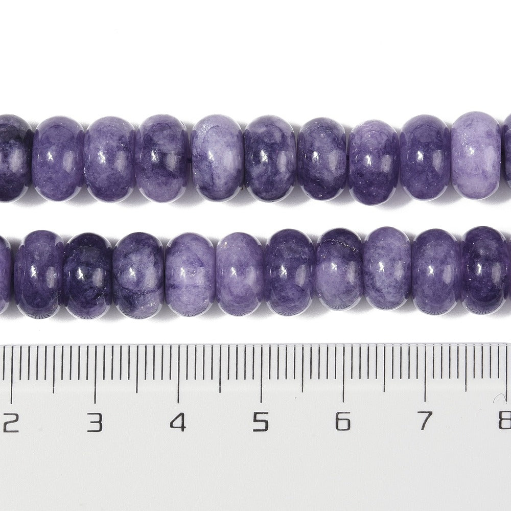zoomed in sections of light purple dyed jade rondelle strand above clear ruler over white surface. 