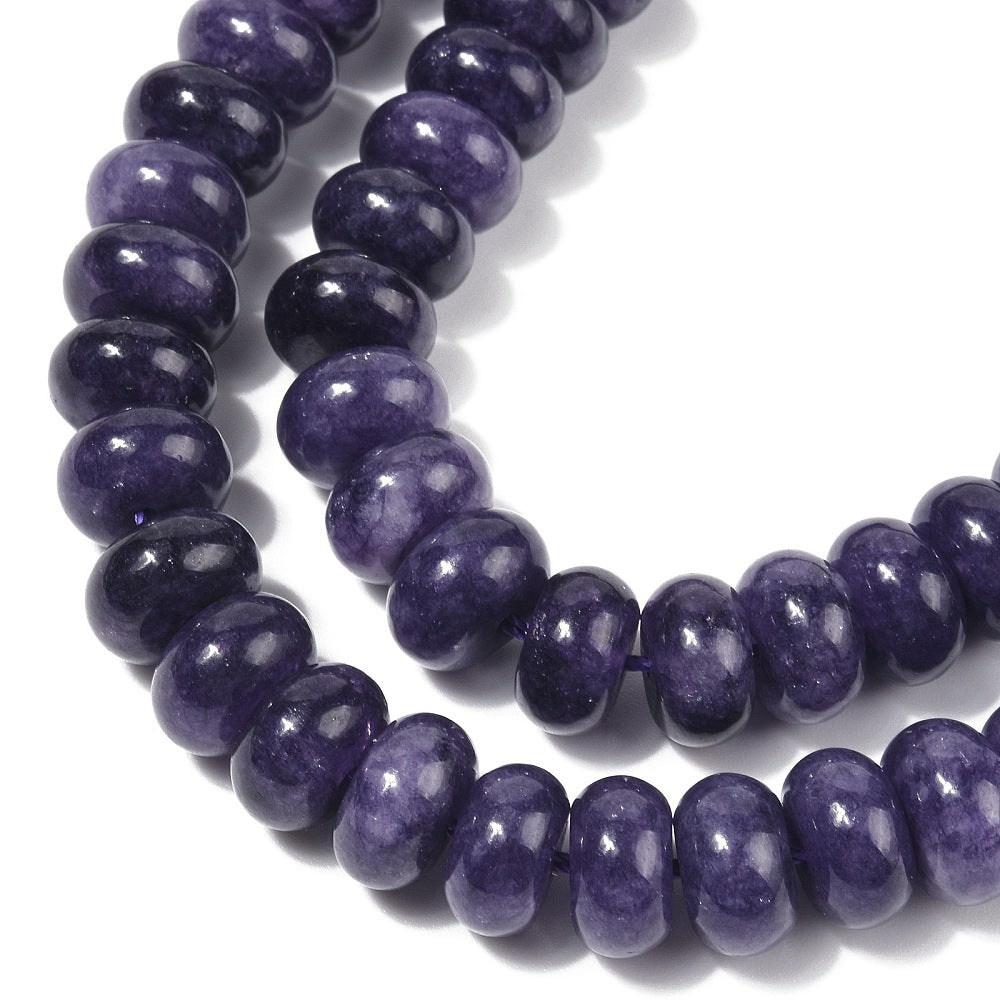 zoomed in sections of dark purple dyed jade rondelle strand over white surface.