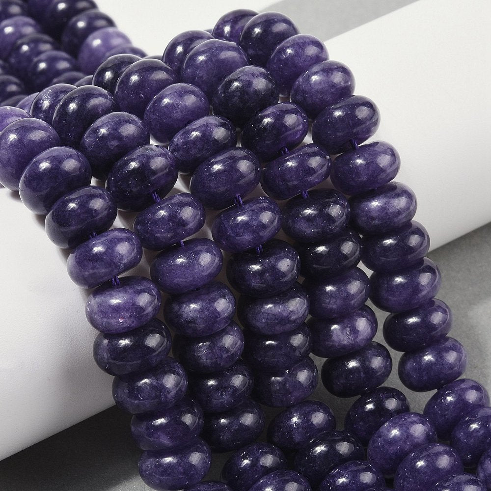 dark purple dyed jade rondelle strands draped over white ledge onto grey surface.