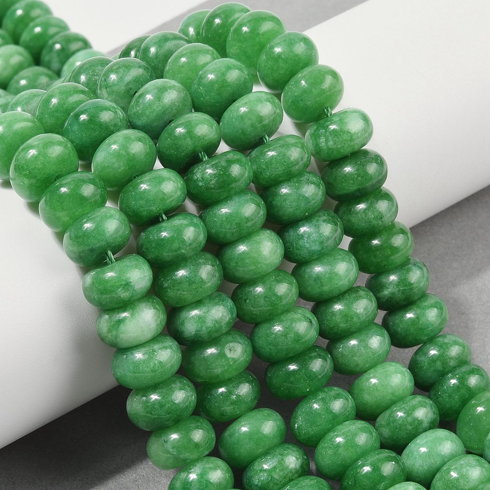 green dyed jade rondelle strands draped over white ledge onto grey surface.