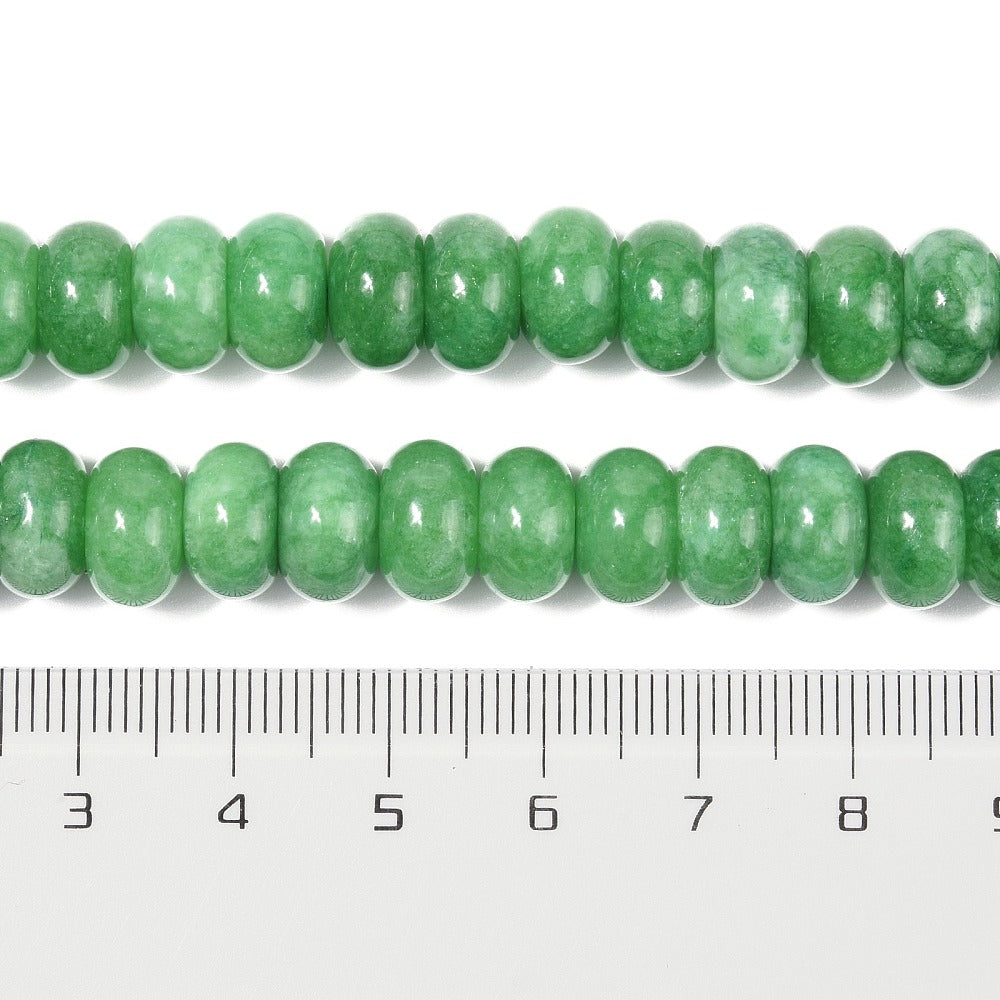 zoomed in sections of green dyed jade rondelle strand above clear ruler over white surface. 