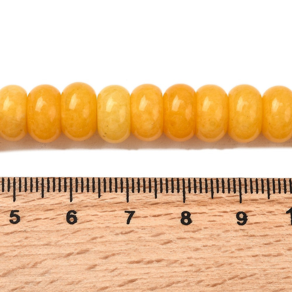 zoomed in section of yellow dyed jade rondelle strand above wooden ruler over white surface. 