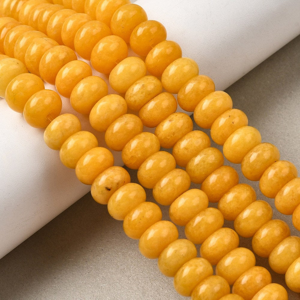 yellow dyed jade rondelle strands draped over white ledge onto tan surface. 