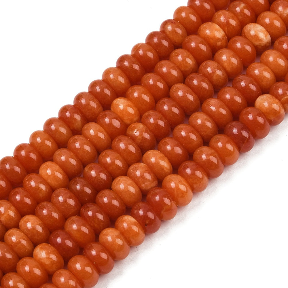 zoomed in sections of orange dyed jade rondelle strands over white surface. 