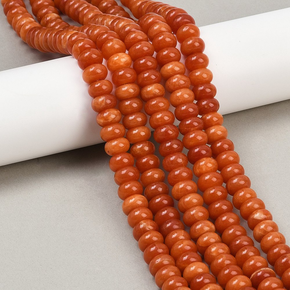 orange dyed jade rondelle strands draped over white ledge onto grey surface.
