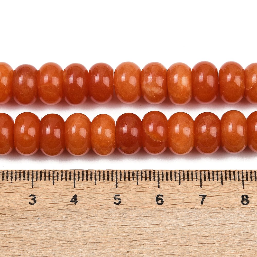 zoomed in sections of orange dyed jade rondelle strand above wooden ruler over white surface. 