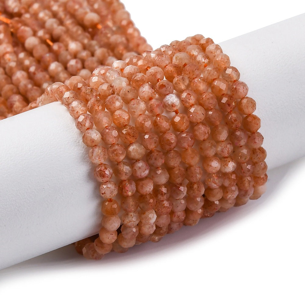 zoomed in sections of multiple faceted round sunstone bead strands wrapped around white cylinder form over white background.