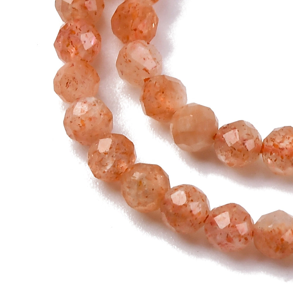 zoomed in sections of faceted round sunstone bead strands over white background.