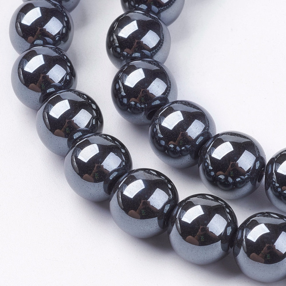 zoomed in sections of round hematite bead strand over white surface. 