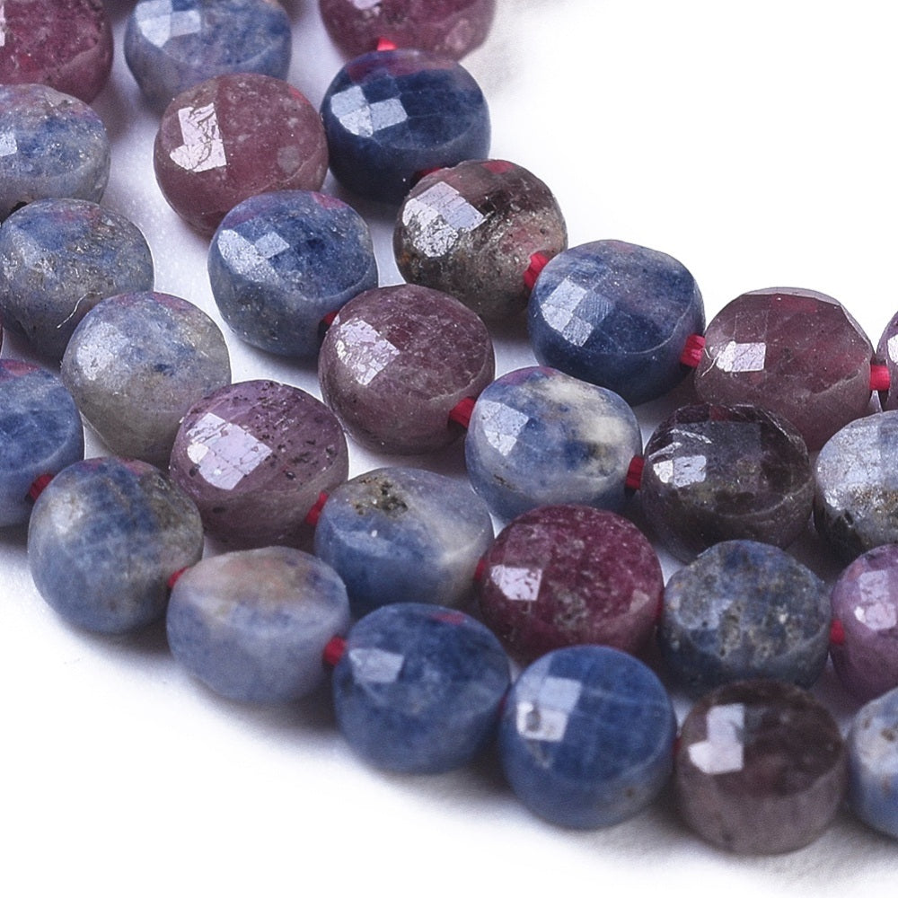 close-up of faceted coin shaped natural ruby and sapphire bead strand over white background. 