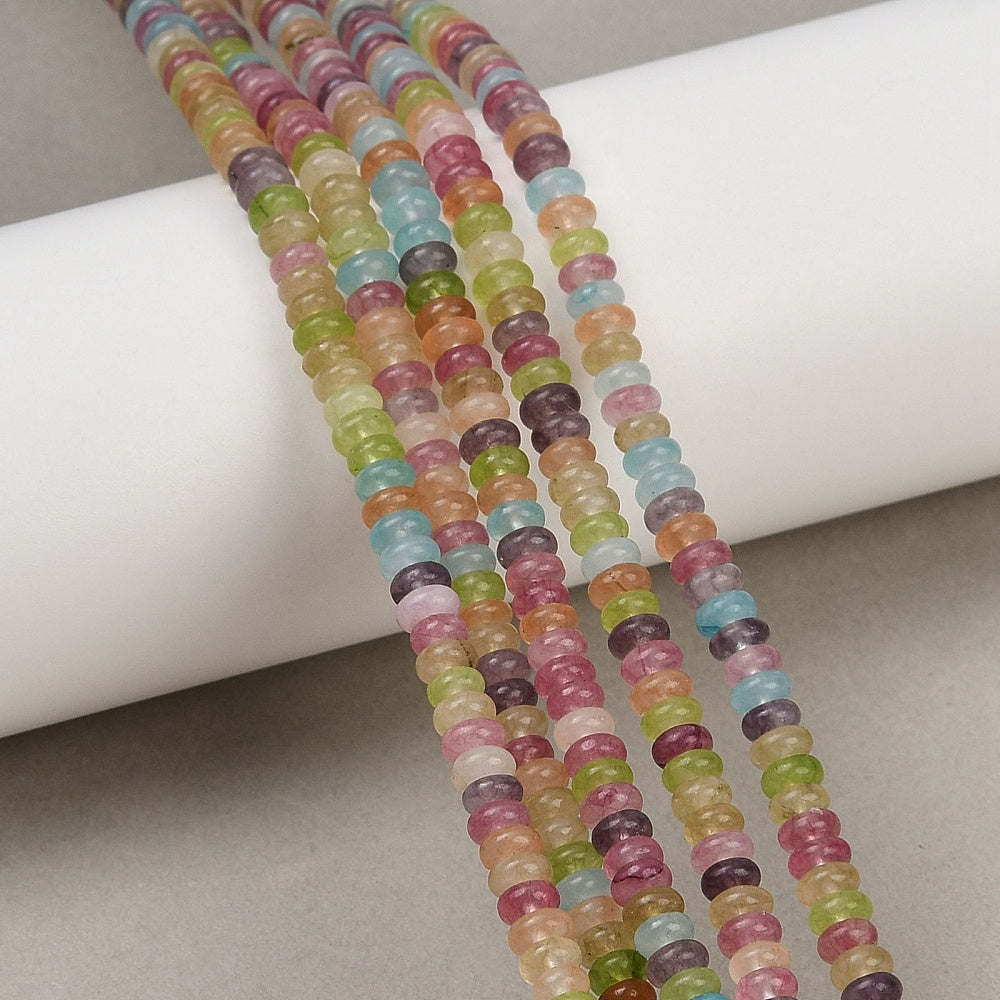 five multicolor dyed jade smooth rondelle bead strands draped over white cylinder form onto tan felt surface. 