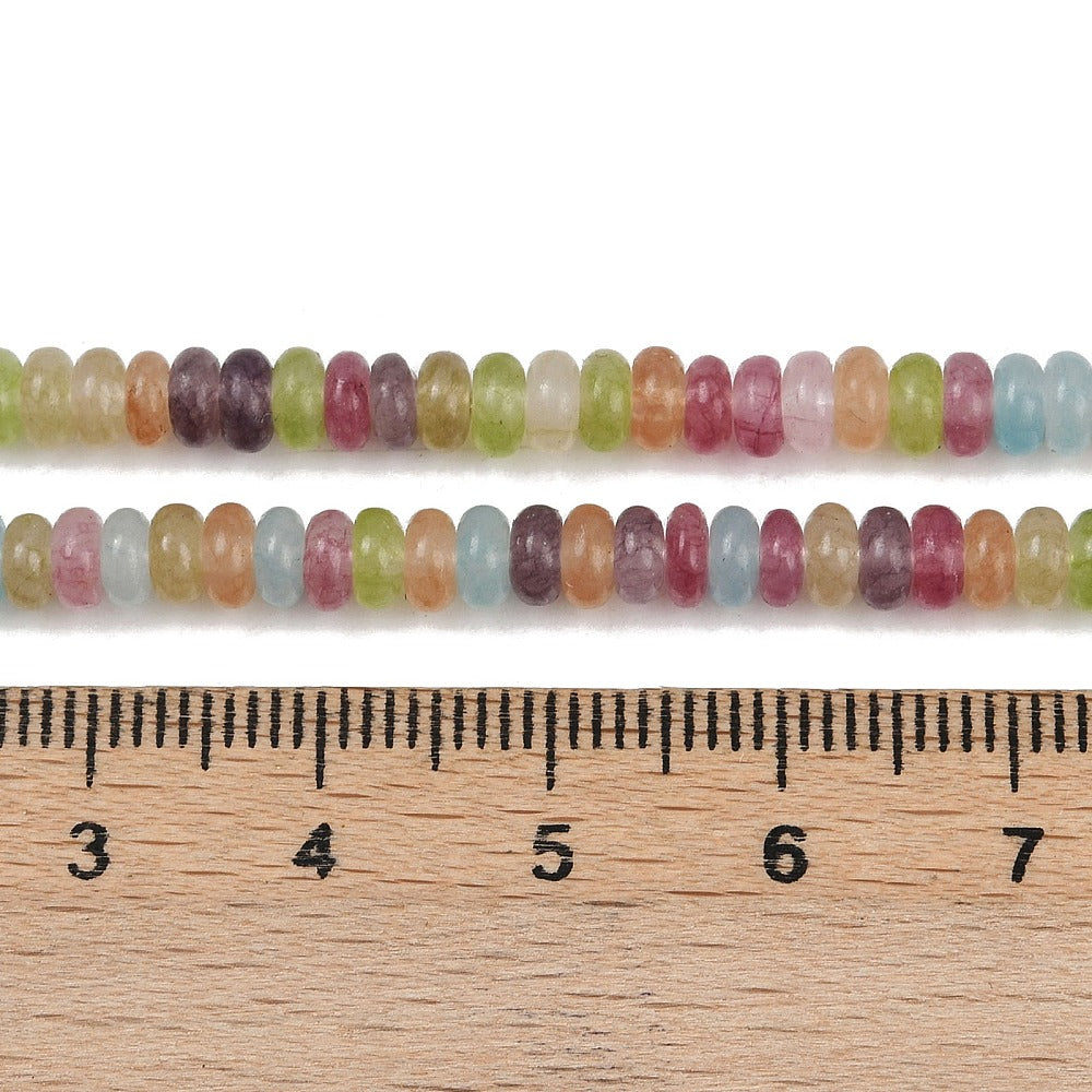 zoomed in sections of multicolor dyed jade smooth rondelle bead strand above wooden ruler over white surface. 