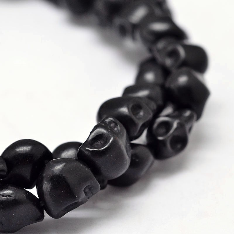zoomed in section of black skull carved stone bead strand on white background. 