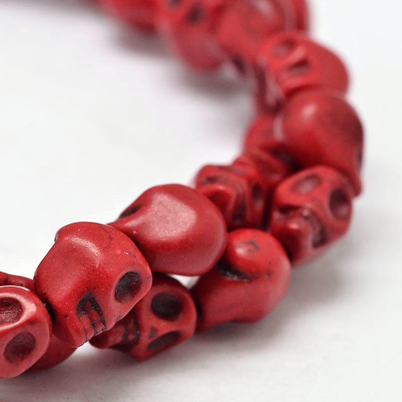 zoomed in section of red skull carved stone bead strand over white background. 
