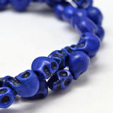 zoomed in section of blue skull carved stone bead strand over white background. 