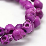 zoomed in section of magenta skull carved stone bead strand over white background. 