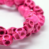 zoomed in section of pink skull carved stone bead strand on white background. 