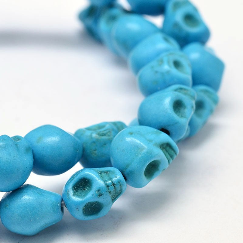 zoomed in section of turquoise skull carved stone bead strand over white background. 