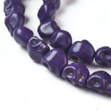 zoomed in section of purple skull carved stone bead strand over white background. 